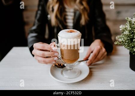 Cropped unkenntlich trendy schöne blonde Frau trinkt aus einem Glas köstlichen Schaum Kaffee Stockfoto