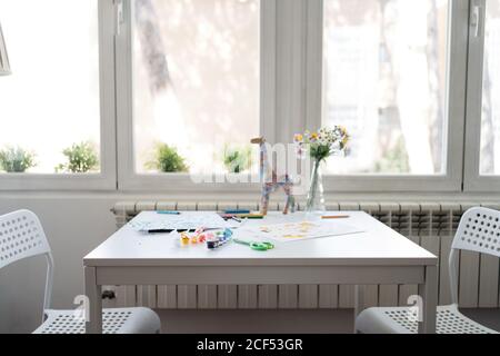 Aquarellpalette mit Buntstiften und bunten Kinderzeichnungen Weißer Tisch mit Stühlen an den Seiten auf Holzboden Stockfoto