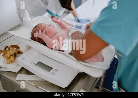 Von oben Seitenansicht des Pflanzenarztes Gewichtung Neugeborenen Baby im modernen Krankenhaus Stockfoto