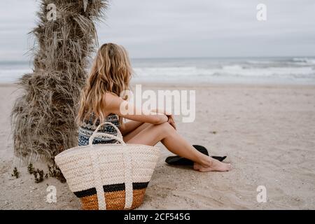 Seitenansicht einer anonymen jungen, schönen blonden Frau, die am Strand sitzt und wegschaut Stockfoto