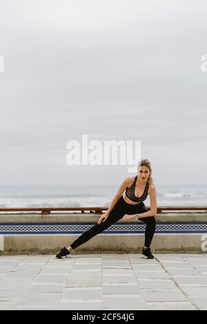 Motivierte, sportliche Frau in aktiver Kleidung, die die Beine im Stehen dehnt, während sie wegschaut Stockfoto