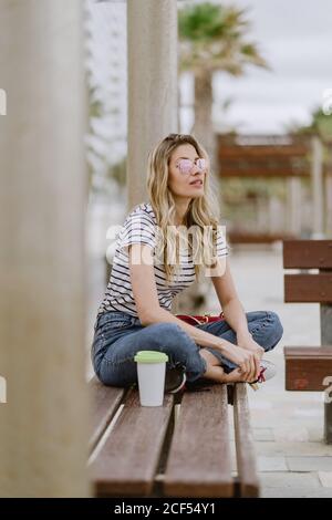 Fröhliche Casual junge Frau sitzt auf der City Bank am Meer Am Sommertag wegschauen Stockfoto