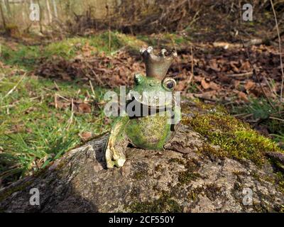 Objet Trouve, ein beschädigtes bizarres Keramikmodell eines gekrönten Frosches, der verlassen auf einem Felsen im sonnenbeschienenen Waldgebiet Cumbria, England, gefunden wurde Stockfoto