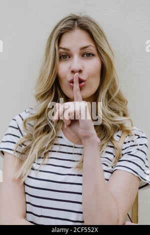 Attraktive junge Frau mit langen schönen Haaren tragen lässig gestreift hemd mit Schweigeschild mit Finger auf den Lippen Stockfoto