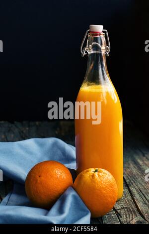 Eine Flasche frischen Zitronensaft in der Nähe von frischen Orangen Auf einem dunklen rustikalen Holztisch mit dunklem Hintergrund Stockfoto