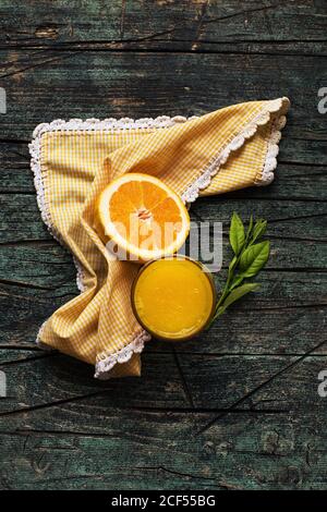 Ein Glas frisch gepresster Orangensaft in der Nähe von einer halben frischen Schneiden Sie Orangen auf einem hölzernen dunklen rustikalen Tisch auf einem Dunkler Hintergrund Stockfoto