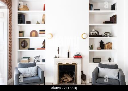 Komfortable graue Sitze in der Nähe von Kamin und Bücherregal in gemütlich Wohnzimmer in stilvoller Wohnung Stockfoto