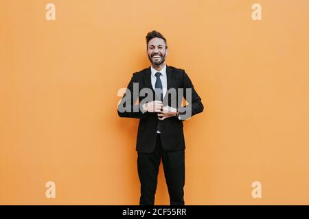 Erwachsene hübsch elegant Geschäftsmann in formelle Anzug Anpassung Jacke und Blick auf die Kamera in der Nähe der orangefarbenen Wand Stockfoto