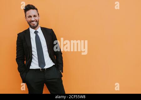 Erwachsene hübsch elegant Geschäftsmann in formellen Anzug Blick auf Kamera In der Nähe der orangefarbenen Wand Stockfoto