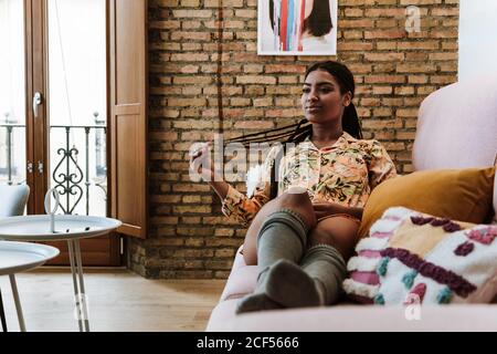 Glückliche ethnische Frau, die im Wohnzimmer sitzt Stockfoto