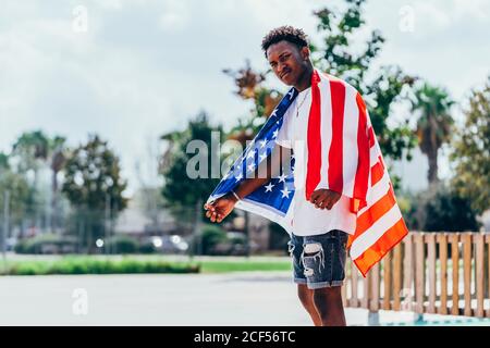 Serious afroamerikanischen Mann hält amerikanische Flagge auf der Schulter und Wegschauen Stockfoto