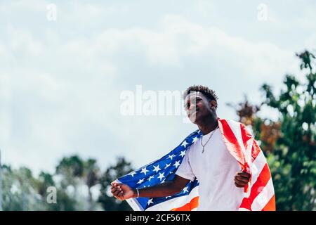 Serious afroamerikanischen Mann hält amerikanische Flagge auf der Schulter und Wegschauen Stockfoto