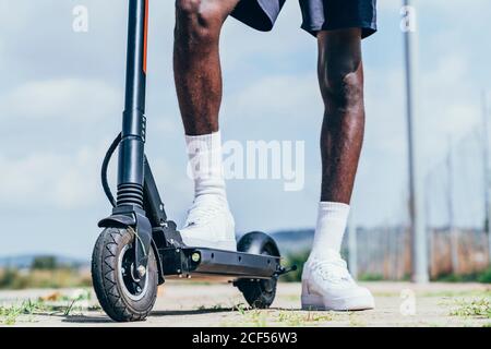 Von unten afroamerikanischen sportlichen Mann Reiten auf Elektroroller In hellen bewölkten Tag Stockfoto