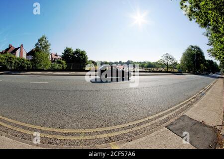 Fischaugen-Objektivansicht eines vorbeifahrenden Autos auf der langen und geraden Bury New Road in Prestwich, Manchester, gegen das Licht aufgenommen (contre-jour) Stockfoto