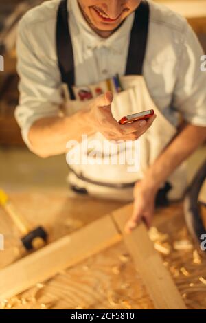 Tischler SMS jemand auf seinem Smartphone in der Nähe von Kreissäge in einem staubigen workshop Stockfoto
