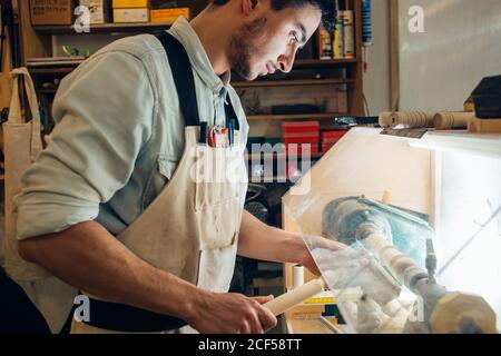 Die Hände des Mannes halten den Meißel in der Nähe der Drehmaschine, der Mann arbeitet an einer kleinen Holzdrehmaschine, ein Handwerker schnitzt ein Stück Holz mit einer Handdrehmaschine Stockfoto