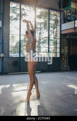 Seitenansicht der jungen anmutigen Ballerina in bunten Bodysuit und Punkte tanzen auf Zehenspitzen während des Trainings im Lichtstudio Stockfoto