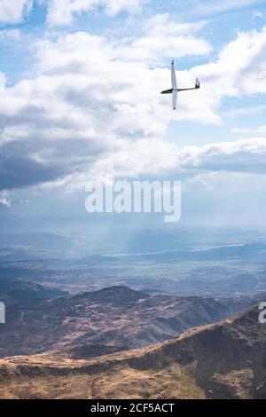 Kleines Segelflugzeug, das über felsige Berge in bewölktem Himmel fliegt Im Sommer sonniger Tag in Wales Stockfoto