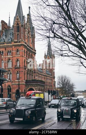 Schwarze Taxis fahren entlang der Asphaltstraße vor dem mittelalterlichen Backsteingebäude Am grauen Regentag in der Stadt Stockfoto