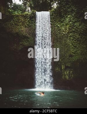 Seitenansicht des Mannes, der im klaren Wasser des Sees mit Wasserfall im Hintergrund schwimmend ist, Bali Stockfoto