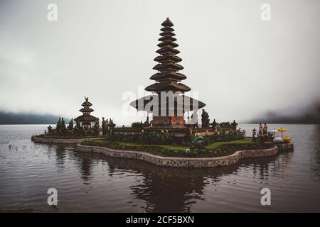 Kleiner Komplex von Gebetspagode mit grünem Garten um im Wasser am Ufer gegen Nebel gebaut, Bali Stockfoto