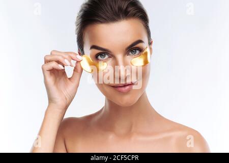 Junge Frau, die goldene Hyaluronic-Hydrogel-Flecken unter den Augen, isoliert auf weißem Hintergrund. Hautpflege, Beauty-Behandlung zur Verringerung Schwellungen Stockfoto