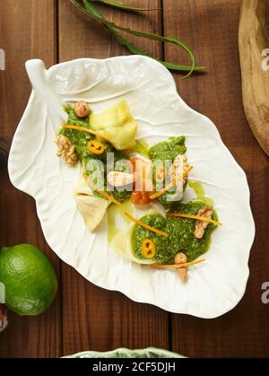 Blick von oben auf handwerkliche Ravioli Pasta mit Kräutersauce serviert Und Muttern auf Blatt geformten Platte auf Holztisch Stockfoto