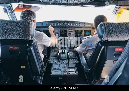 Rückansicht des männlichen Piloten und des CO-Piloten mit Instrument Panel im Cockpit der modernen Passagierflugzeuge während des Fluges Stockfoto