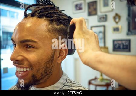 Crop-Ansicht der anonymen Friseur tun einen modernen Haarschnitt zu Ein fröhlicher afroamerikanischer Kunde Stockfoto