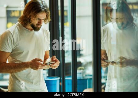 Junger bärtiger hübscher Mann mit Mobiltelefon und Nachrichtenfunktion Auf Spiegelfläche Stockfoto
