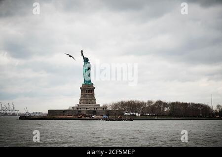 Low-Angle-Ansicht der berühmten Freiheitsstatue in New York City gegen grau bewölkten Himmel mit Vogel fliegen in der Nähe Stockfoto