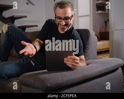 Entspannter Mann, der auf dem Tablet lächelt, allein auf dem Sofa im Wohnzimmer zu Hause Stockfoto