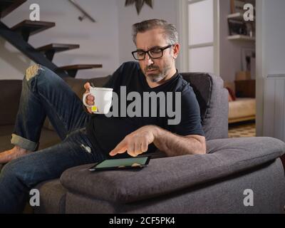 Entspannter Mann, der im Internet surfte und alleine einen Tee tranken konnte Das Sofa im Wohnzimmer zu Hause Stockfoto