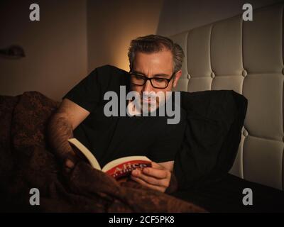 Entspannter Mann im Bett, der vor dem Schlafen und ein Buch liest Ruhe Stockfoto