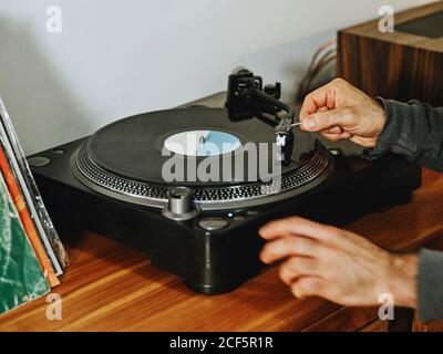 Beschnittene unerkennbare Person Einstellung Plattenspieler und genießen Songs auf Retro Vinylscheibe beim Abkühlen zu Hause Stockfoto