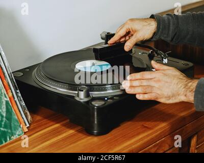 Beschnittene unerkennbare Person Einstellung Plattenspieler und genießen Songs auf Retro Vinylscheibe beim Abkühlen zu Hause Stockfoto