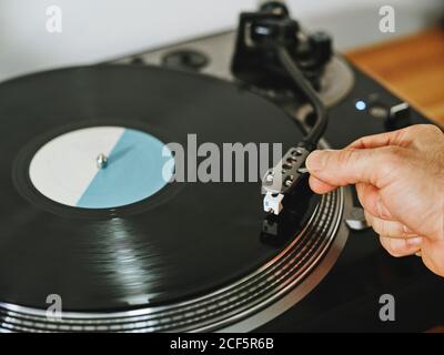 Von oben beschnittene Personenhände, die eine zeitgenössische Vinyl-Platte anpassen Player mit Retro-Disc auf Holztisch platziert Stockfoto