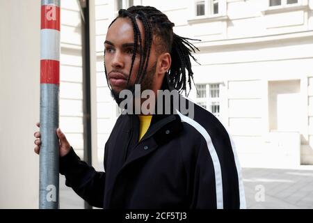 Junge afroamerikanische Mann mit geflochtenen Haaren halten Stange und Blick weg auf städtischen Hintergrund Stockfoto