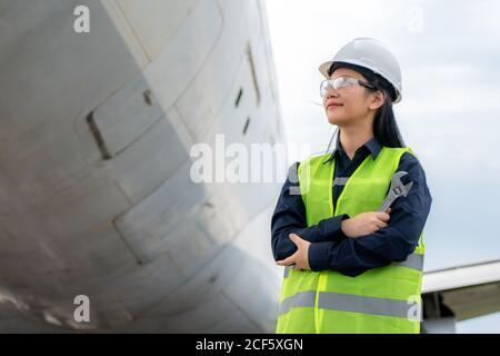 Asiatische Frau Ingenieur Wartung Flugzeug Arm gekreuzt und hält Schraubenschlüssel vor Flugzeug von Reparaturen, Fixes, Modernisierung und Renovierung in Flughafen Stockfoto