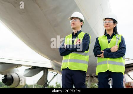 Asian Mann und Frau Ingenieur Wartung Flugzeug Arm gekreuzt und hält Schraubenschlüssel vor Flugzeug von Reparaturen, Fixes, Modernisierung und Renovierung i Stockfoto