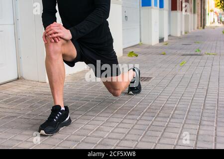 Gesichtslose Jogginghose in Sportkleidung zum Aufwärmen Stretching Beine gelehnt Auf dem Knie Vorbereitung auf joggen in der städtischen Straße Stockfoto