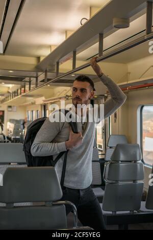 Konzentrierter junger Mann mit Rucksack, der den Handlauf hält, während er im Platz steht Leeres U-Bahn-Auto Stockfoto