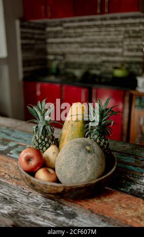 Holzschale mit frischer Melone, Äpfeln und Ananas auf der Sommerterrasse von Bali Stockfoto