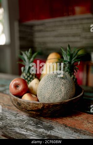 Holzschale mit frischer Melone, Äpfeln und Ananas auf der Sommerterrasse von Bali Stockfoto