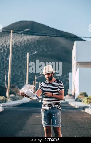 Junge trendige Mann auf der Suche Ziel auf der Karte, während Sie auf der Straße gegen Berg Hintergrund in La Restinga, El Hierro Stockfoto