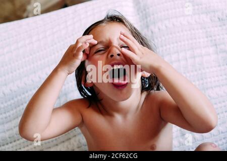 Kind ohne Kleidung sitzt auf dem Sofa und macht Gesichter Stockfoto