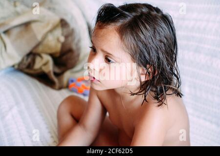 Kind ohne Kleidung sitzt auf dem Sofa und schaut weg Stockfoto