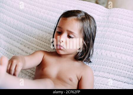 Kind ohne Kleidung sitzt auf dem Sofa und schaut weg Stockfoto