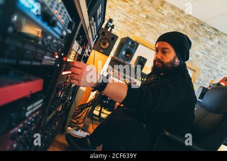 Ein Musiker, der in einem Studio arbeitet, während er die Stereosteuerung für Musik anpasst Stockfoto