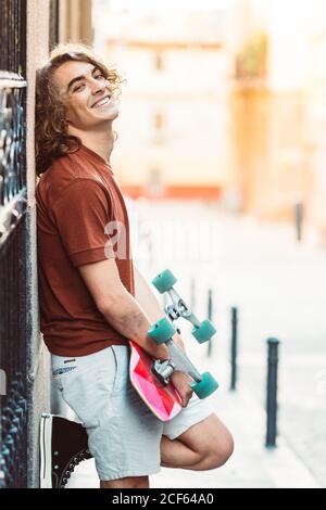 Schöner sportlicher Mann hält Longboard, während er im Sommer in der Stadt steht City Street Stockfoto